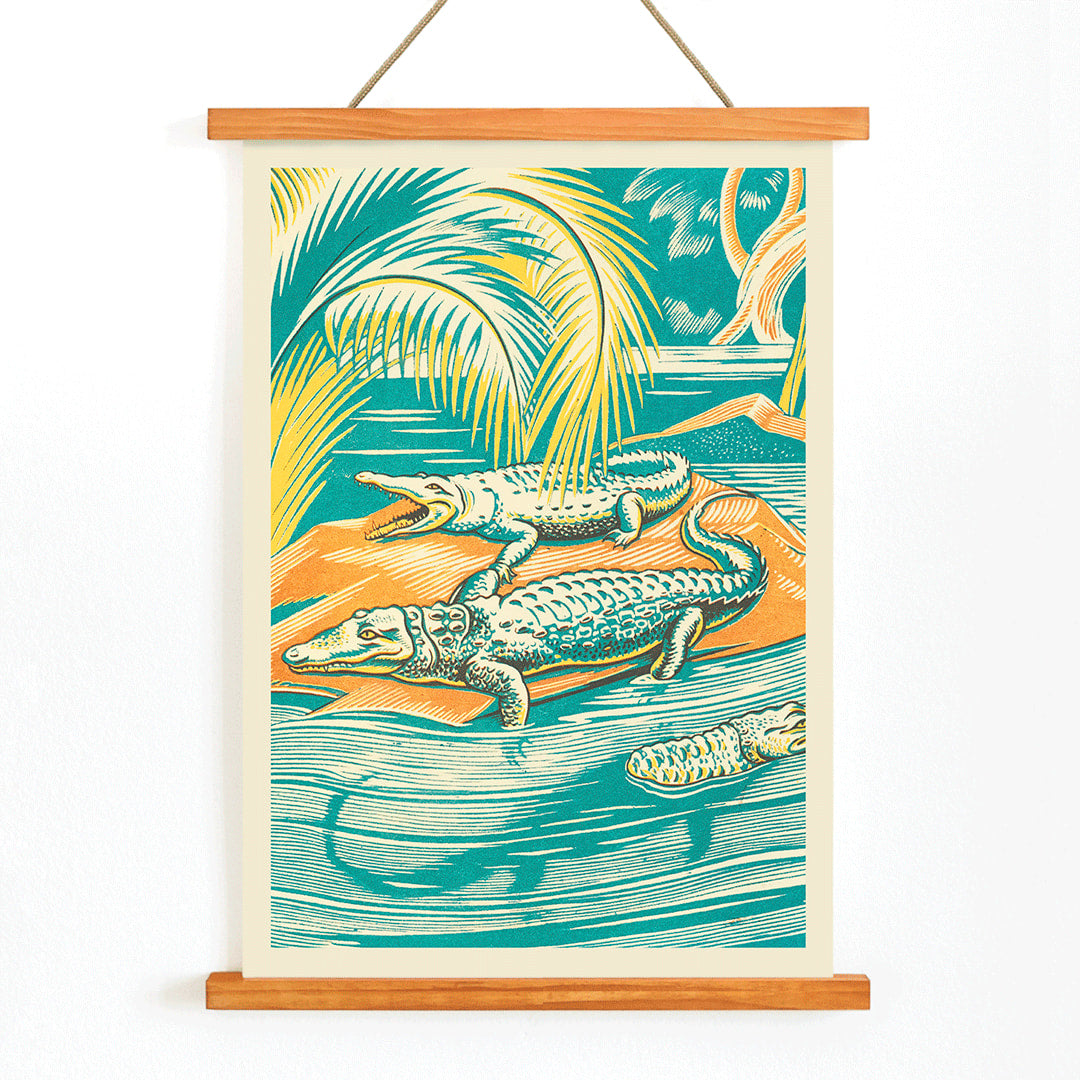 A Jungle Picnic Pl.03 Crocodile by Clifford Webb vibrant jungle artwork and poster showing crocodiles resting by a river under palm trees, with wooden magnetic frame on white background