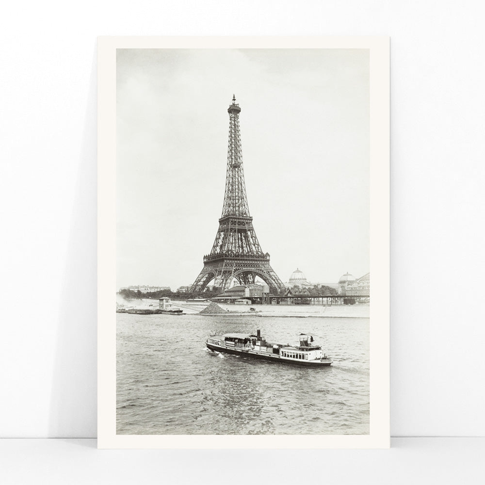 Black and white photograph and poster of the Eiffel Tower in Paris with a vintage boat on the Seine river wall decor artwork, framed and displayed in modern living room decor