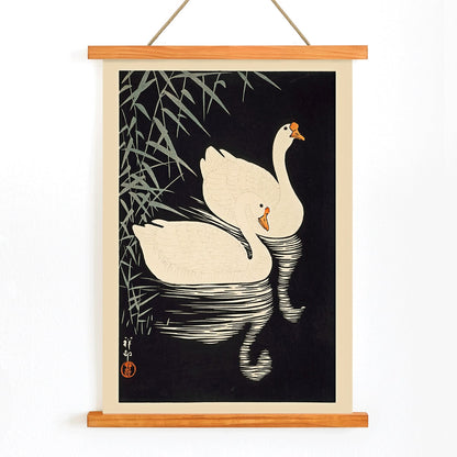 White Chinese Geese Swimming by Ohara Koson featuring two elegant white geese on water with bamboo leaves and reeds poster artwork, with wooden magnetic frame on white background