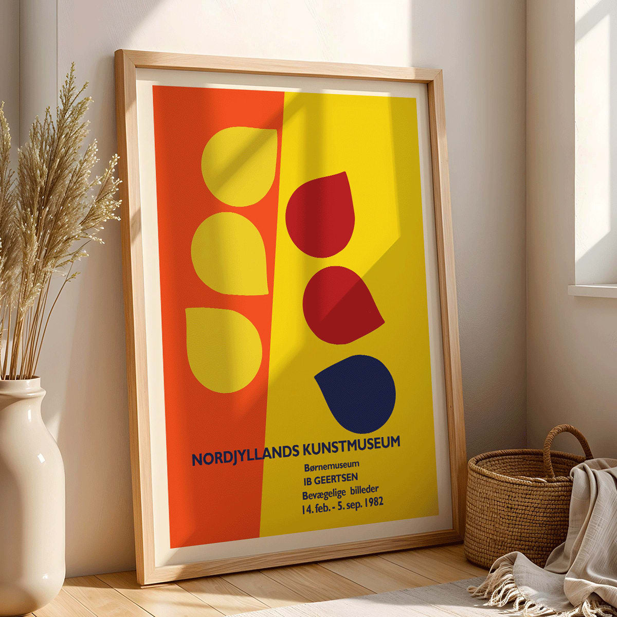 Exhibition poster by Ib Geertsen with colorful geometric shapes in yellow red and blue on an orange and yellow background, framed and displayed in modern living room decor