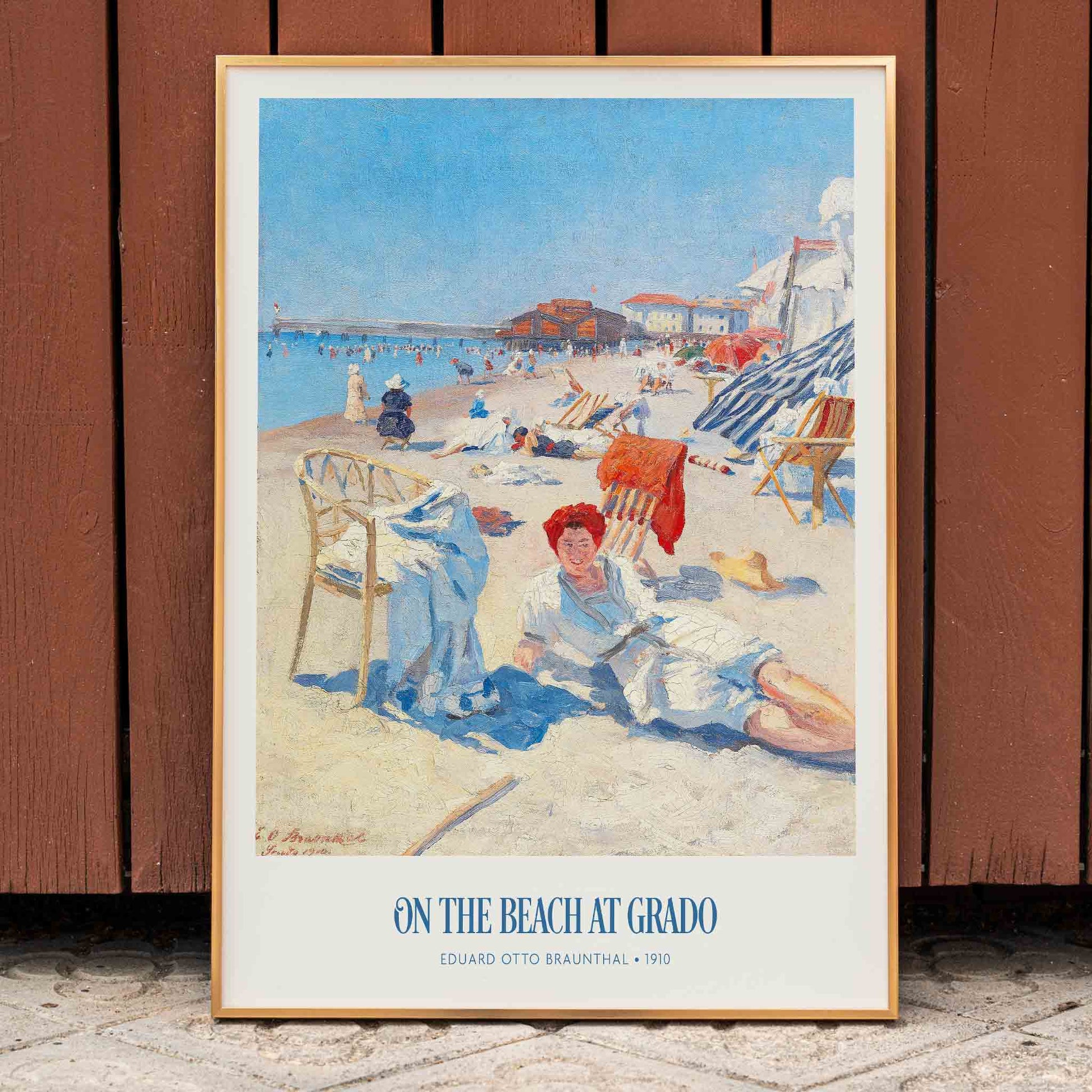 People relaxing on a sunny beach with chairs buildings and colorful umbrellas On the Beach at Grado by Eduard Otto Braunthal, framed and displayed in home decor